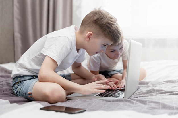 Jungenbrüder sitzen auf dem Bett vor einem Laptop. Fernunterricht.