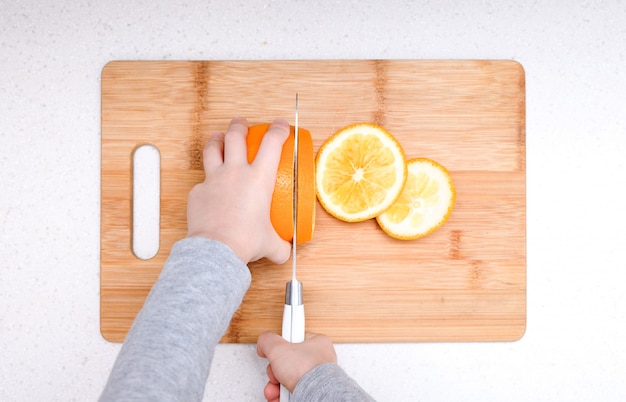 Jungenhände, die frische Orange auf Küche schneiden