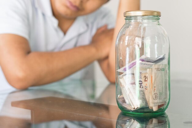 Jungenhand neben seinen Ersparnissen in einem Glas junger Mann neben seinen persönlichen Finanzen, gelangweilter Student
