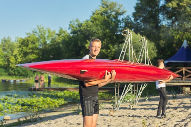 Jungenjugendliche, die mit Sportboot Kajak zum Fluss gehen