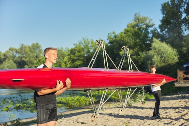 Jungenjugendliche, die mit Sportboot Kajak zum Fluss gehen