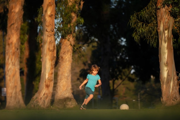 Jungenkind, das Fußball auf Fußballplatz spielt. Kind, das Fußball spielt. Kind spielt Fußball auf dem Spielplatz im Park.