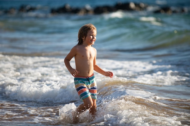 Jungenkind, das in Meereswellen springt, springt durch Wassermeerspritzer Sommerkinderurlaub