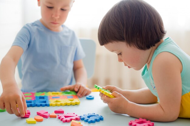 Jungenmädchen sammeln weiches Puzzlespiel bei Tisch