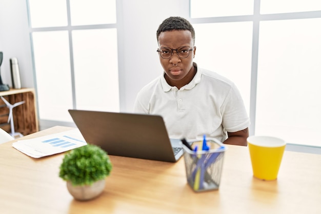 Junger afrikaner, der im büro mit computer-laptop arbeitet, ist skeptisch und nervös, runzelt die stirn und verärgert wegen des problems. negativer Mensch.