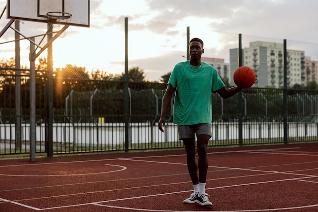 Junger afrikanisch-amerikanischer Basketballspieler, der mit Ball läuft und versucht, Slam Dunk außerhalb des Spielens zu erzielen