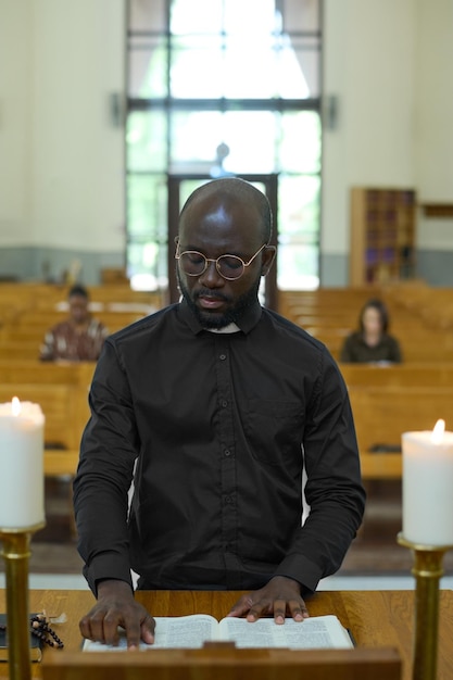 Junger afrikanisch-amerikanischer Mann in schwarzem Hemd mit Bürokragen, der Evangelium liest