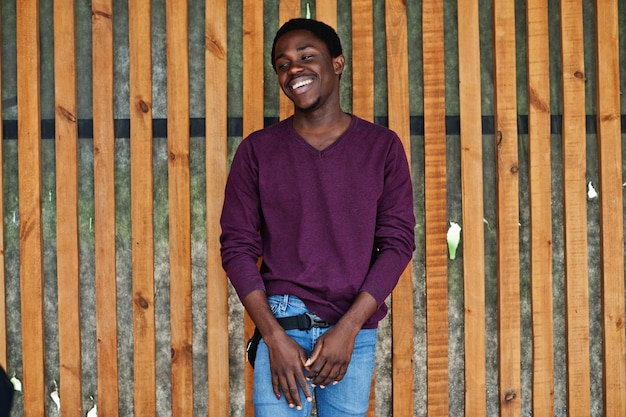 Junger afrikanisch-amerikanischer Mann in violettem Pullover posierte gegen Holzwand