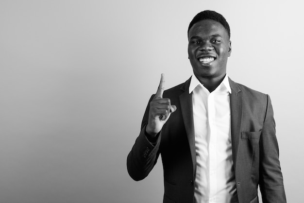 junger afrikanischer Geschäftsmann, der Anzug gegen weiße Wand trägt. Schwarz und weiß