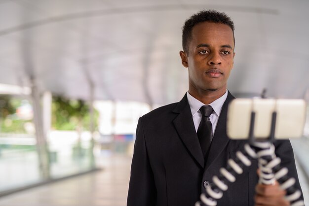 Junger afrikanischer Geschäftsmann, der Handy und Vlogging im Freien in der Stadt verwendet