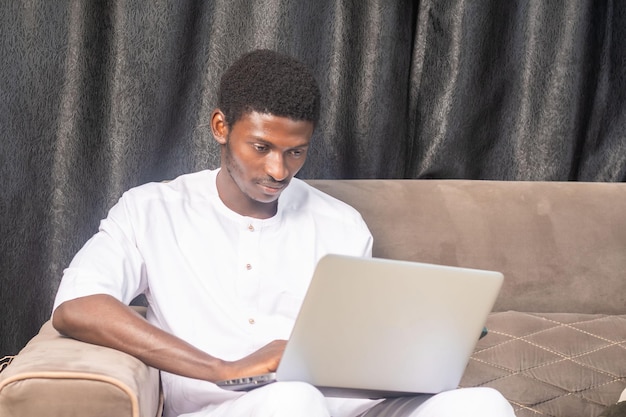 Junger afrikanischer Geschäftsmann sitzt und arbeitet an seinem Laptop
