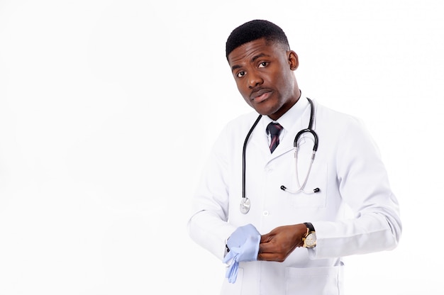 Junger afrikanischer gutaussehender Arzt auf Weiß, der mit Phonendoskop isoliert wird, zieht medizinische Handschuhe an