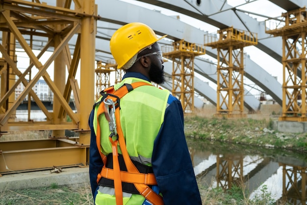 Junger afrikanischer Ingenieur, der auf der Baustelle steht und riesige Rahmen betrachtet