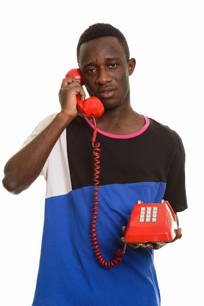 Junger afrikanischer Mann, der am alten Telefon spricht, das müde schaut