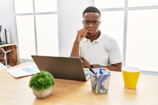 Junger afrikanischer mann, der im büro arbeitet und computer-laptop-mund und lippen als reißverschluss mit den fingern schließt. geheim und still, tabu reden