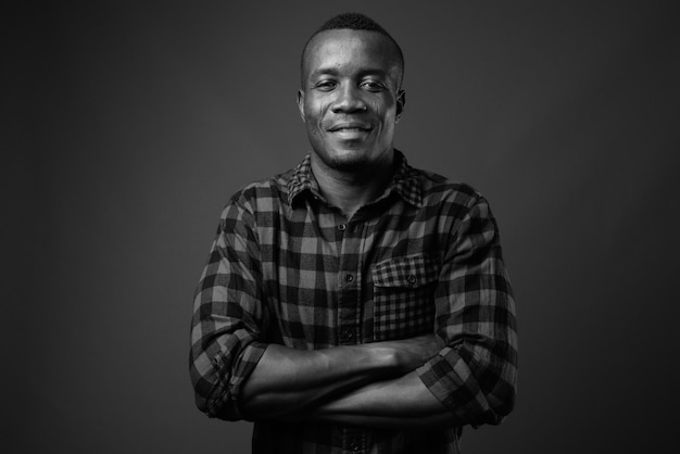 junger afrikanischer Mann, der kariertes Hemd gegen graue Wand trägt. Schwarz und weiß