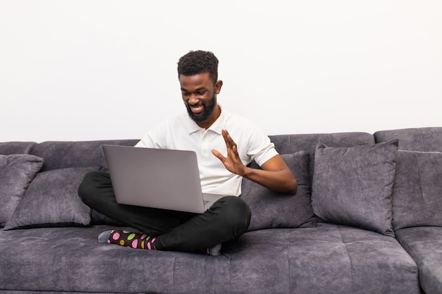 Junger afrikanischer Mann, der Video-Chat auf Laptop im Wohnzimmer verwendet