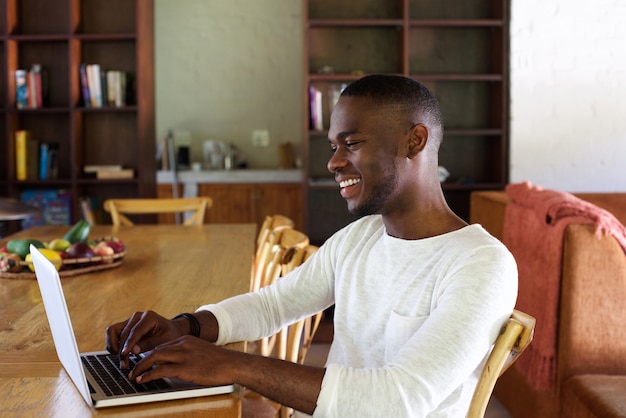 Junger afrikanischer Mann, der zuhause an Laptop arbeitet