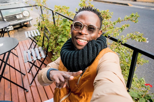 Junger afrikanischer mann im freien, der glücklich lächelnd ein selfie macht, das v-zeichen mit der hand macht