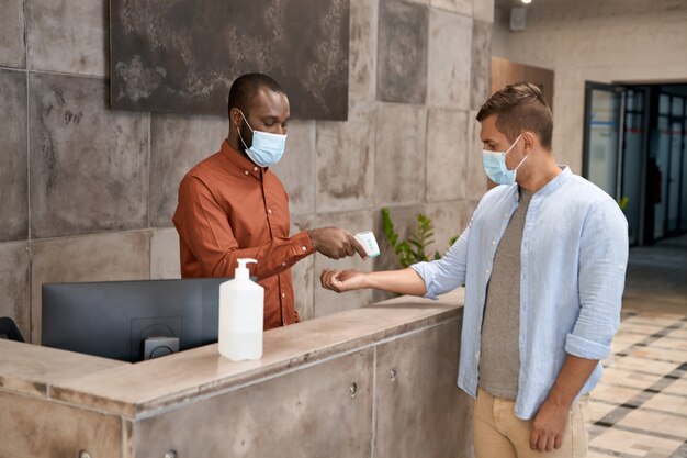 Junger afrikanischer Mann mit medizinischer Maske, der an der Rezeption im modernen Büro steht und misst