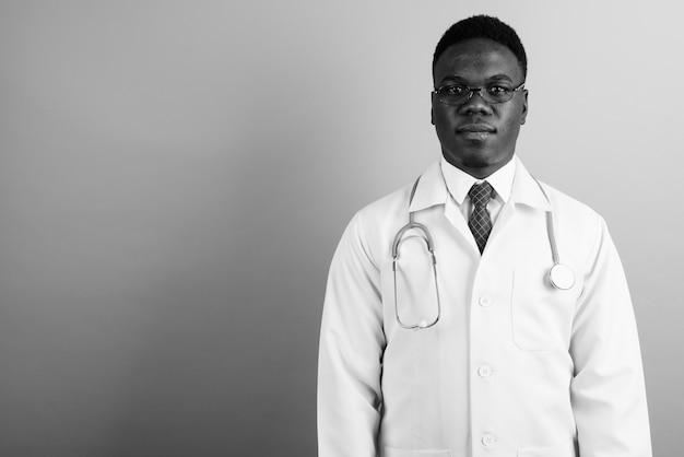 junger afrikanischer Mannarzt, der Brillen gegen weiße Wand trägt. Schwarz und weiß