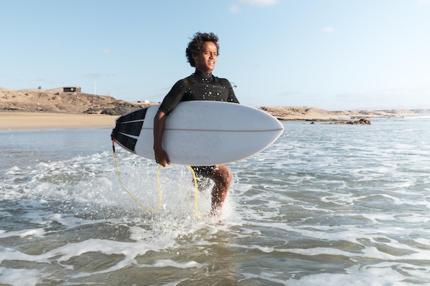 Junger afrikanischer Surfer am Strandufer, der zu den Wellen läuft