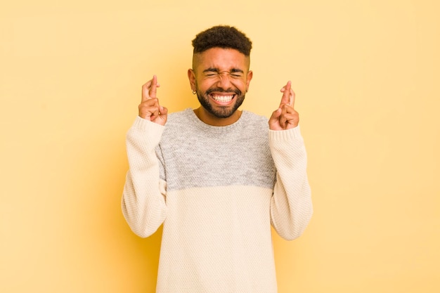 Junger afro-mann, der lächelt und ängstlich beide daumen drückt, sich besorgt fühlt und viel glück wünscht oder hofft