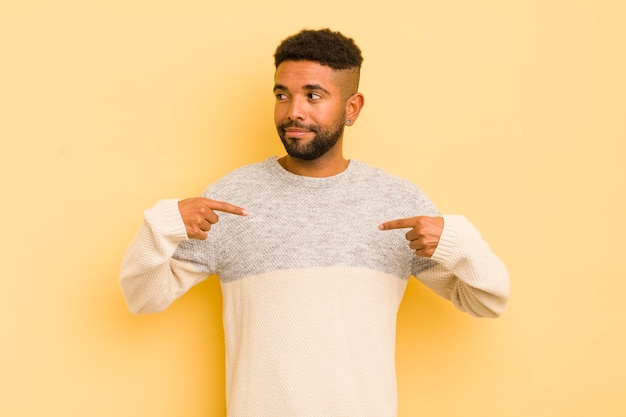 Junger afro-mann, der stolz positiv und lässig aussieht und mit beiden händen auf die brust zeigt