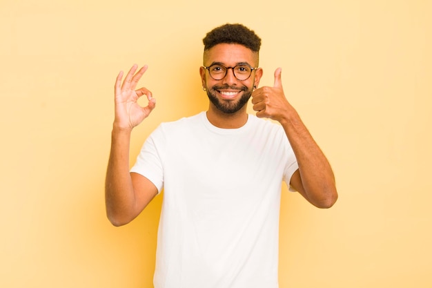 Junger Afro-Mann fühlt sich glücklich, erstaunt, zufrieden und überrascht, zeigt okay und Daumen hoch Gesten lächelnd