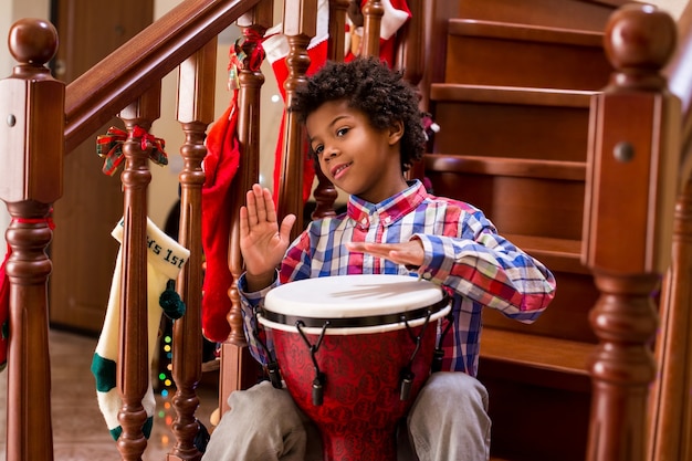 Junger Afro-Schlagzeuger auf Treppen freundliches Afro-Kind mit Trommel, die Djembe wie ein Profi spielt kostenlose Weihnachten ...