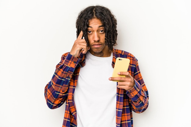Junger Afroamerikaner hält Handy isoliert auf weißem Hintergrund und zeigt mit Fingerdenken auf eine Aufgabe