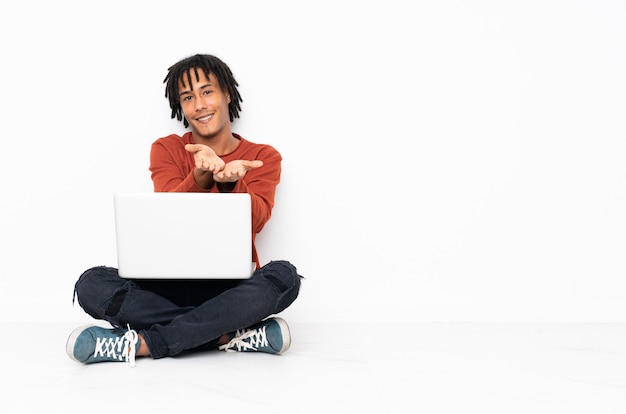 Junger Afroamerikanermann, der auf dem Boden sitzt und mit seinem Laptop arbeitet, der Leerraum hält