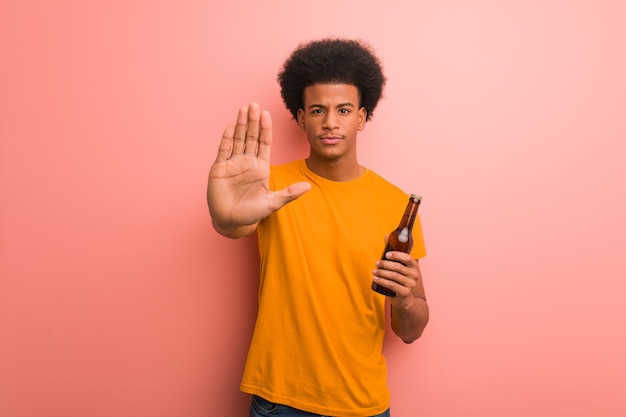 Junger Afroamerikanermann, der ein Bier hält, das Hand vor setzt