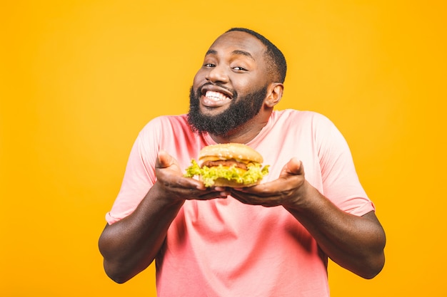 Junger Afroamerikanermann, der Hamburger isst, der über gelber Wand lokalisiert wird.