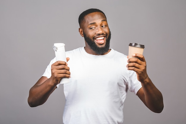 Junger Afroamerikanermann, der Wahl zwischen Tasse Kaffee und Recycling eines steht über lokalisiertem grauem Hintergrund macht.
