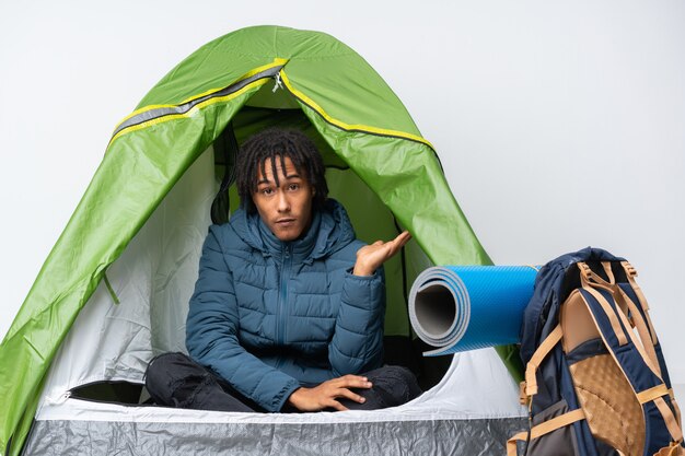 Foto junger afroamerikanermann in einem grünen zelt des campings, das zweifel gestikuliert