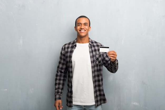 Junger Afroamerikanermann mit dem karierten Hemd, das eine Kreditkarte hält