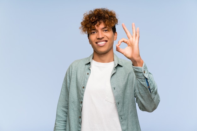 Junger Afroamerikanermann über der lokalisierten blauen Wand, die okayzeichen mit den Fingern zeigt