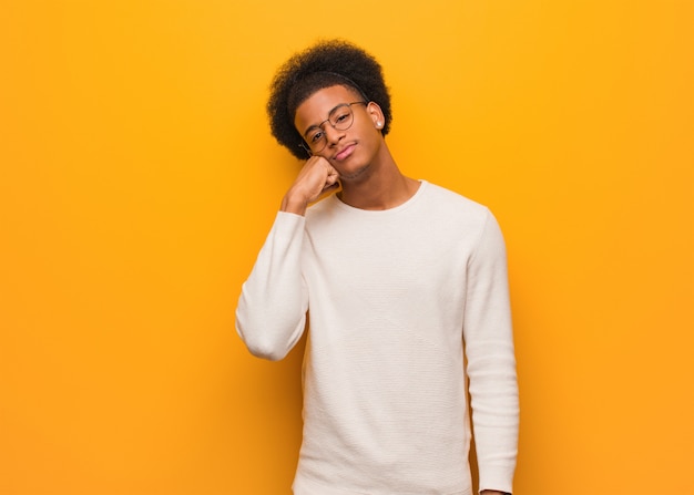 Junger Afroamerikanermann über einer orange Wand denkend an etwas, schauend zur Seite