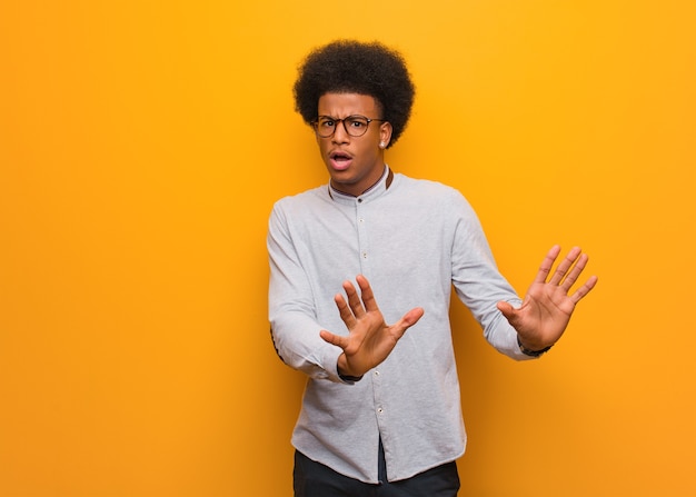 Junger Afroamerikanermann über einer orange Wand, die etwas ablehnt, das eine Geste des Ekels tut