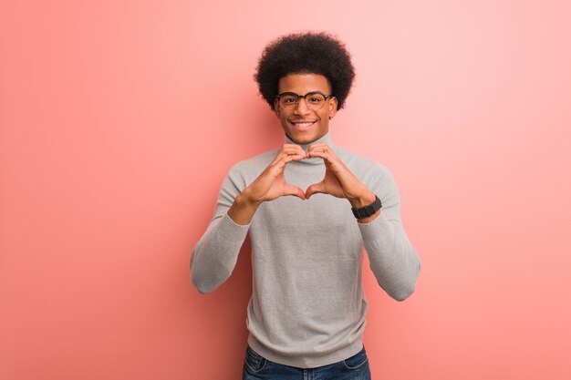 Junger Afroamerikanermann über einer rosa Wand, die eine Herzform mit den Händen tut