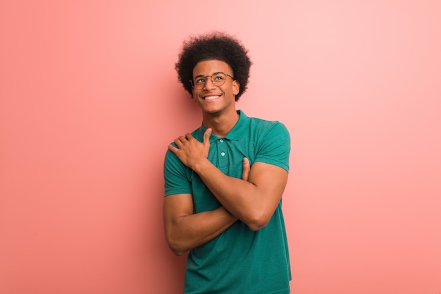 Junger Afroamerikanermann über einer rosa Wand, die eine Umarmung gibt