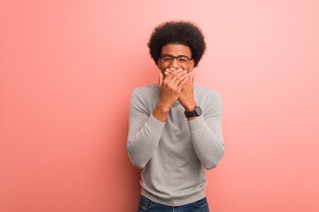 Junger Afroamerikanermann über einer rosa Wand lachend über etwas und bedecken Mund mit den Händen