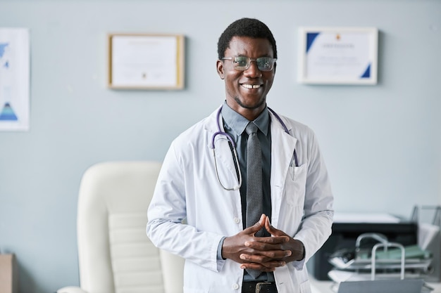 Junger afroamerikanischer Arzt, der im Büro steht und in die Kamera lächelt