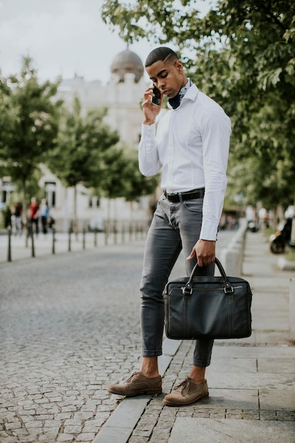 Junger afroamerikanischer Geschäftsmann, der ein Mobiltelefon benutzt, während er auf einer Straße auf ein Taxi wartet