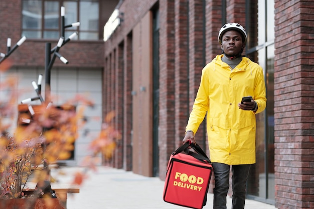 Junger afroamerikanischer Kurier in Helm und gelber Jacke