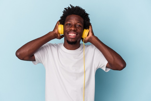 Junger afroamerikanischer Mann, der auf blauem Hintergrund Musik hört, die nach einem Sieg die Faust hebt, Gewinnerkonzept.