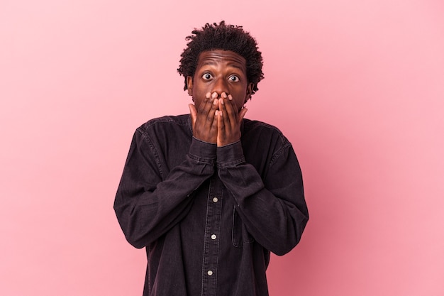Junger afroamerikanischer Mann, der auf rosafarbenem Hintergrund isoliert ist, schockiert, den Mund mit den Händen zu bedecken.