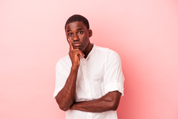 Junger afroamerikanischer Mann, der auf rosafarbenem Hintergrund unglücklich in die Kamera schaut, mit sarkastischem Ausdruck isoliert.