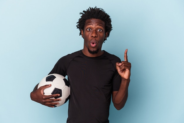 Junger afroamerikanischer Mann, der Fußball spielt, isoliert auf blauem Hintergrund, der eine großartige Idee hat, Konzept der Kreativität.